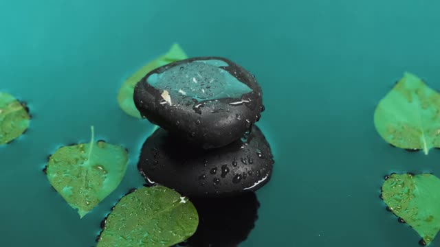 水滴落在石头堆上，树叶漂浮在水面上。视频素材