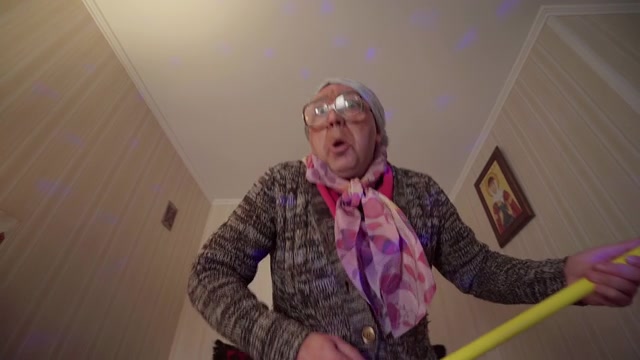 有趣的祖母把拖把弹得像吉他一样。戴着大眼镜的滑稽脸。视频素材画面2