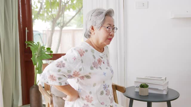 亚洲老年妇女感到疼痛，疼痛，背痛时站在家里和坐在家里，背痛的概念视频素材