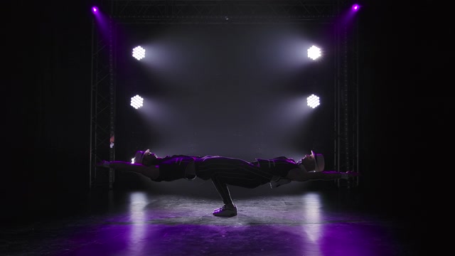两个男子体操杂技演员摆一个平衡姿势。在团队合作中表演复杂戏法的强壮运动员的剪影。在聚光灯下的黑色背景上。慢动作视频素材画面3