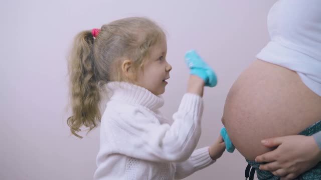 可爱的女孩用蓝色的靴子摸着怀孕的妈妈的肚子视频素材