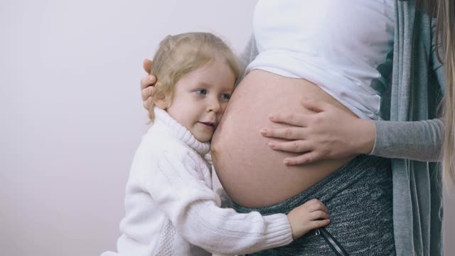 穿着毛衣的女孩在家拥抱怀孕的妈妈亲吻肚子视频素材