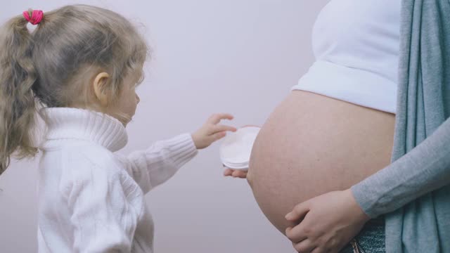 扎马尾的女孩在孕妇的肚子上涂霜视频素材