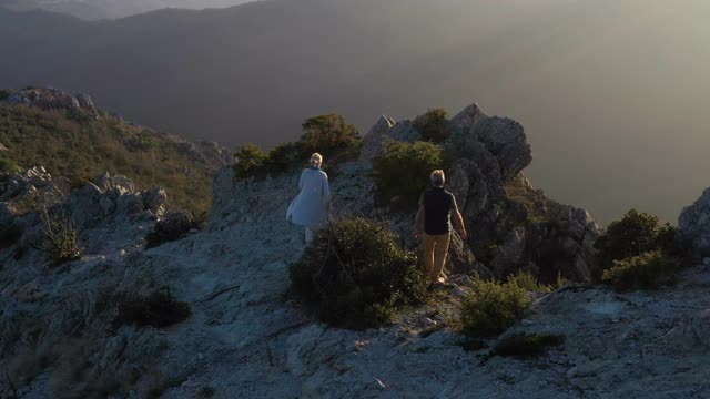 鸟瞰图的成熟夫妇站在崎岖的岩石突出和欣赏日出视频素材