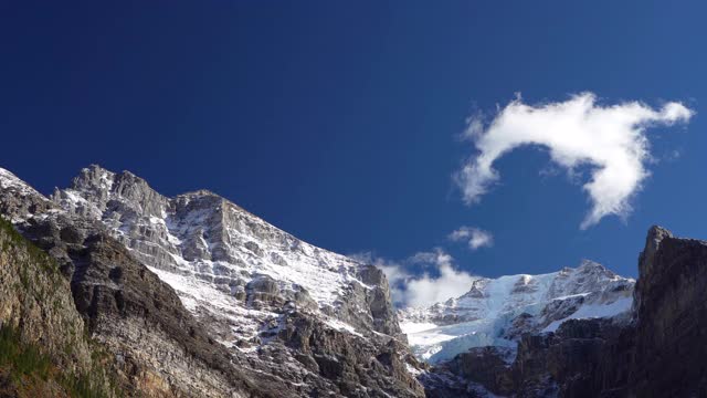 白雪覆盖着雄伟的山峰，深蓝色的天空和流动的云在背景。视频素材