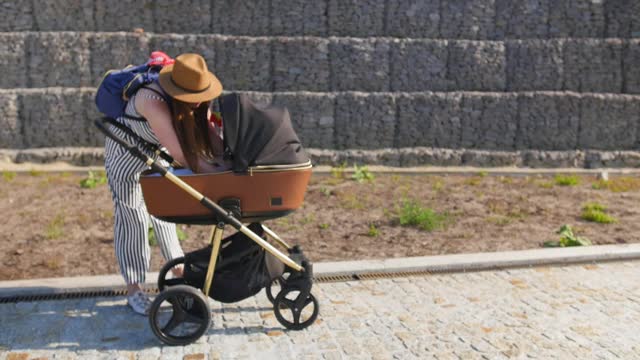 一位年轻的母亲走着，试图把她的孩子从婴儿车里抱出来。家庭、母性和人的观念。全景。视频素材