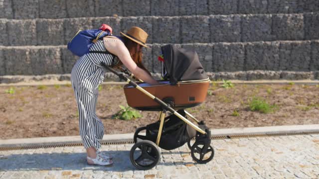 一位年轻的母亲走着，试图把她的孩子从婴儿车里抱出来。家庭、母性和人的观念。全景。视频素材