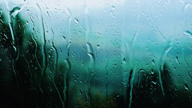 窗外下着雨，雨点顺着玻璃流下，雨点落下背景。视频素材