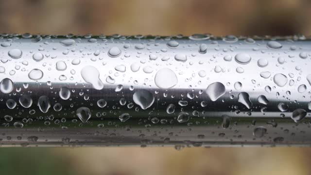 不锈钢扶手上的雨点映衬着模糊的大海背景。特写镜头。雨露上的水滴聚集在闪亮的钢铬杆扶手上视频素材