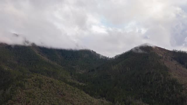 4k空中时间间隔的雾移动在树木覆盖的山峰上视频素材