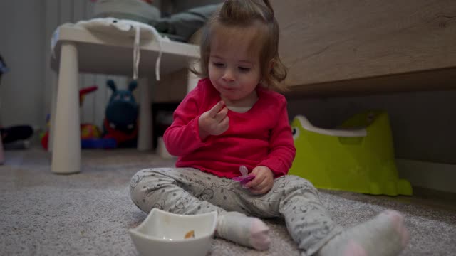 饥饿的小女孩坐在地板上享受着她的零食视频素材