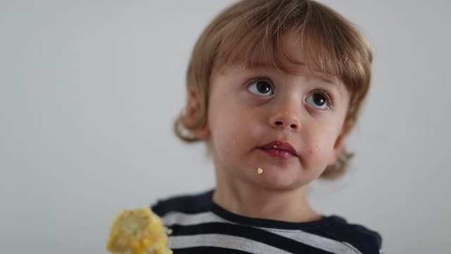 蹒跚学步的孩子正在吃玉米棒。一岁婴儿健康零食视频素材