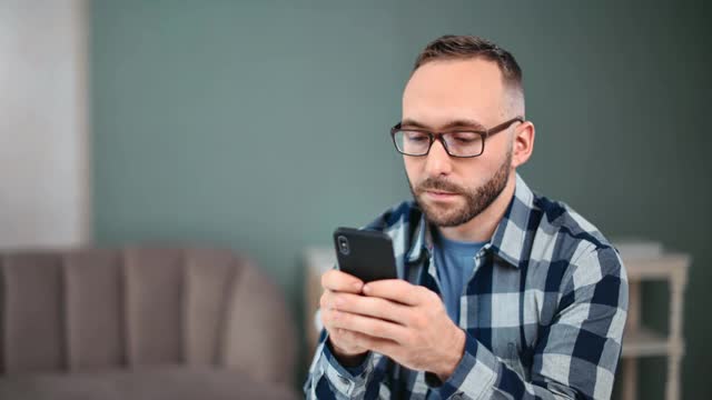 专注的男人聊天短信应用程序在家里使用智能手机。中近距离拍摄4k红色相机视频素材