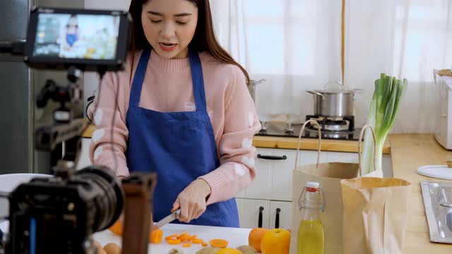 一名亚洲女子在摄像机前录制视频。用相机记录水果和健康饮料的故事给她的订户。视频素材