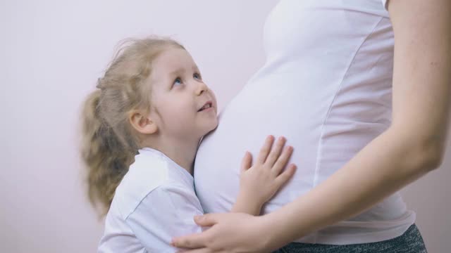 小女孩在房间里轻轻地抚摸着怀孕的妈妈的肚子视频素材