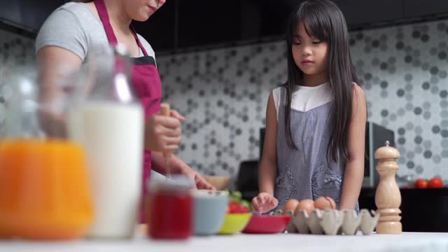 妈妈和可爱的小女儿在厨房里一起准备做煎饼。视频素材