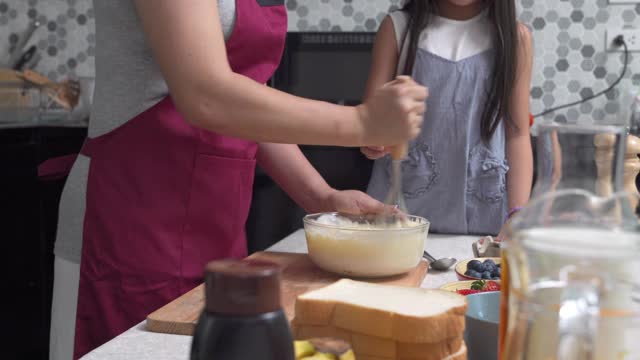 妈妈和可爱的小女儿在厨房里一起准备做煎饼。视频素材