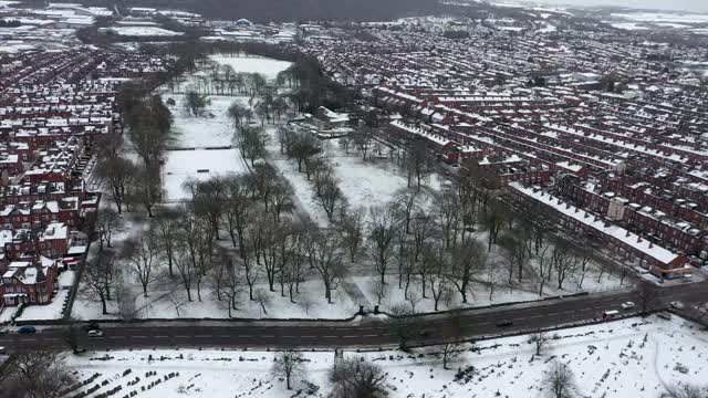 英国利兹市一个下雪天的航拍镜头，显示冬天比斯顿村一排排屋顶被雪覆盖的排屋视频素材