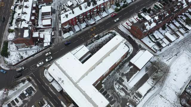 英国利兹市一个下雪天的航拍镜头，显示冬天比斯顿村一排排屋顶被雪覆盖的排屋视频素材