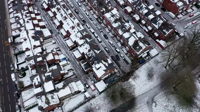 英国利兹市一个下雪天的航拍镜头，显示冬天比斯顿村一排排屋顶被雪覆盖的排屋视频素材