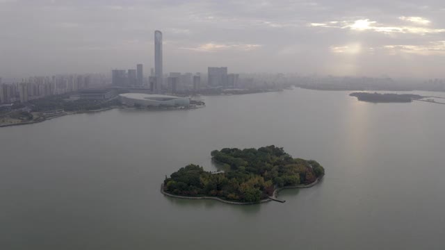 在多云的天空下，航拍拍摄城市附近的金鸡湖上的岛屿，无人机在现代建筑附近飞行——中国苏州视频素材