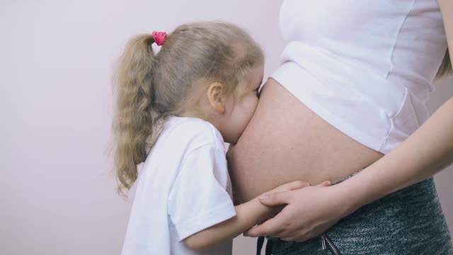 女孩笑着在明亮的房间里玩着怀孕妈妈的肚子视频素材