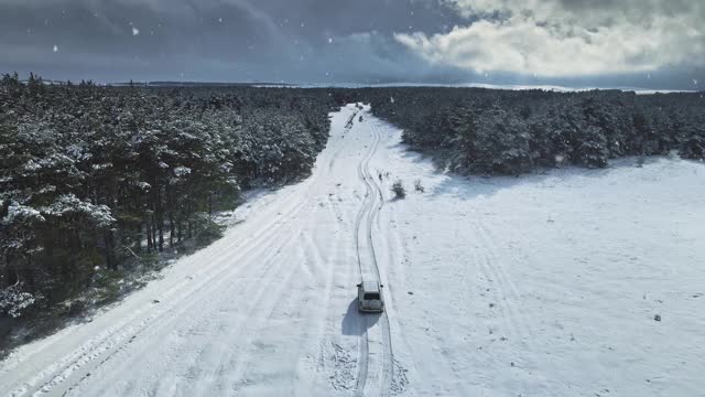 汽车在白雪覆盖的森林周围行驶的鸟瞰图视频素材