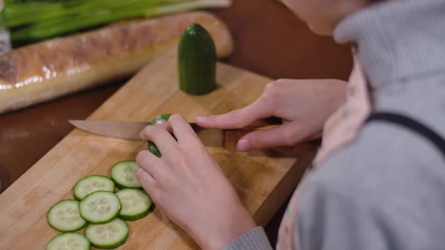 一个面目全非的男孩正在切黄瓜做健康沙拉。高视角儿童烹饪健康饮食在厨房在家。妈妈的手拿着切片品尝。电影4k ProRes总部。视频素材