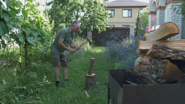 伐木工在夏天的小屋里用斧子劈柴。日志为烧烤或烧烤。男人的工作。有人用大斧子在院子里劈柴。准备烧烤用的柴火视频素材