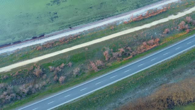 一辆白色汽车在被湖泊包围的乡村公路上行驶的鸟瞰图。视频素材