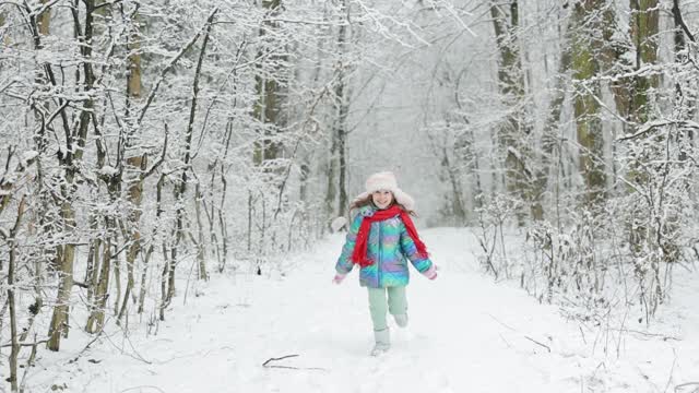 快乐的小女孩在冬天玩雪。女孩喜欢冬天，有霜冻的日子。可爱的小女孩穿着冬天的衣服在雪天里跑步视频素材