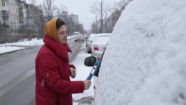 一场大雪过后，这位妇女清理车上的积雪。视频素材