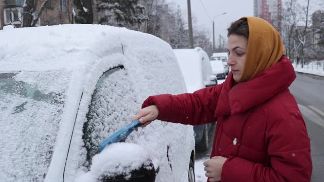 一场大雪过后，这位妇女清理车上的积雪。视频素材