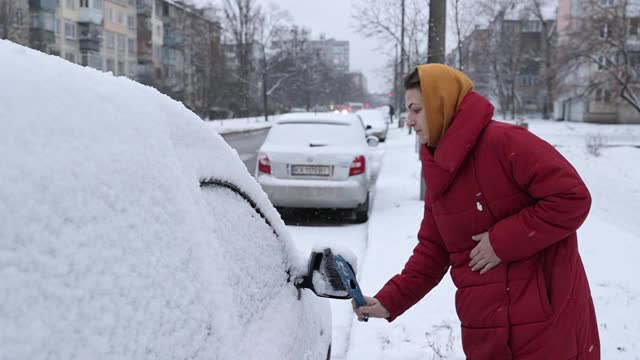 一场大雪过后，这位妇女清理车上的积雪。视频素材