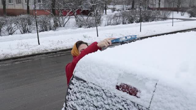 一场大雪过后，这位妇女清理车上的积雪。视频素材