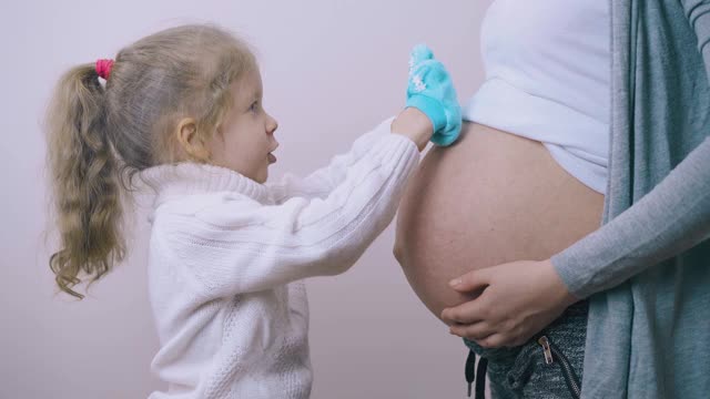 女孩把蓝色婴儿鞋放在怀孕的妈妈的手掌上视频素材