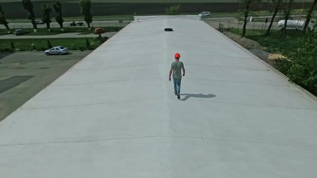 技术专家在建筑物的平屋顶上行走。屋顶上戴着橙色安全帽的男工人正在制定建设太阳能农场的计划。视频素材画面1