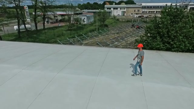 技术专家在建筑物的平屋顶上行走。屋顶上戴着橙色安全帽的男工人正在制定建设太阳能农场的计划。视频素材画面3
