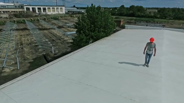 技术专家在建筑物的平屋顶上行走。屋顶上戴着橙色安全帽的男工人正在制定建设太阳能农场的计划。视频素材画面4