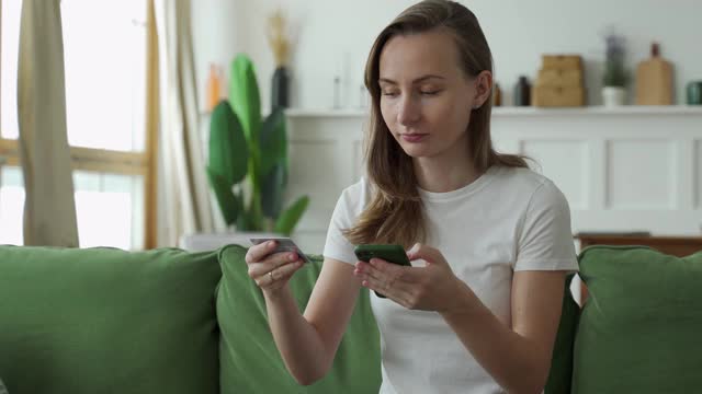 年轻女子坐在家里的沙发上，用信用卡和智能手机在网上购物视频素材