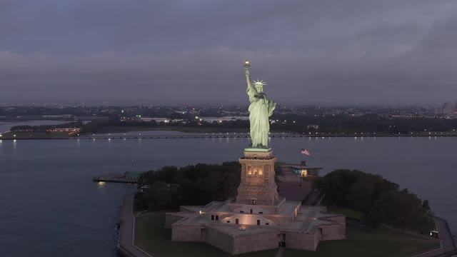 空自由岛与自由女神像在美丽的日出和美国国旗挥舞的背景，鸟瞰图视频素材