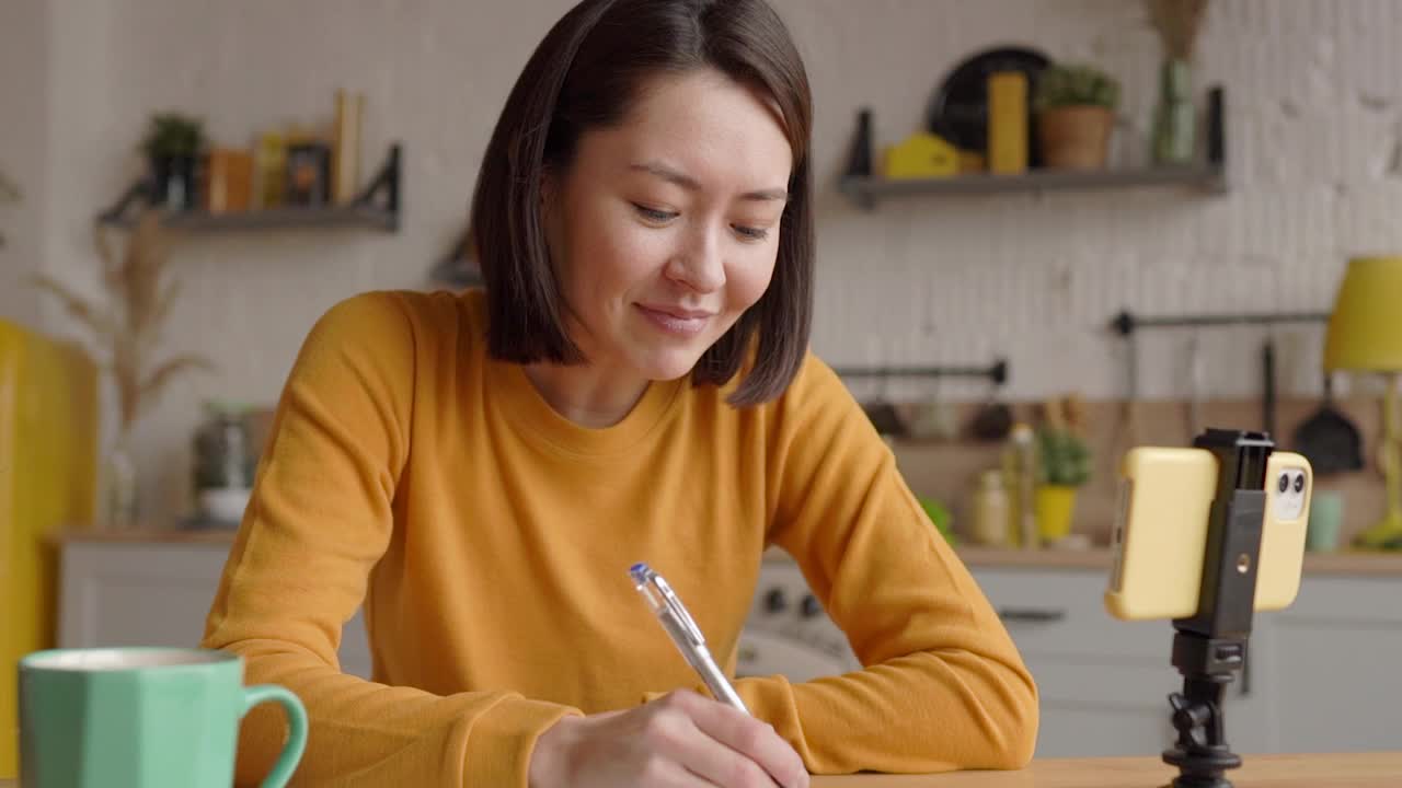 快乐的亚洲年轻女性博主或视频博主坐在家里讲话，看着摄像机说话，做视频会议电话记录，生活方式博客，视频博客在家里做视频聊天视频素材