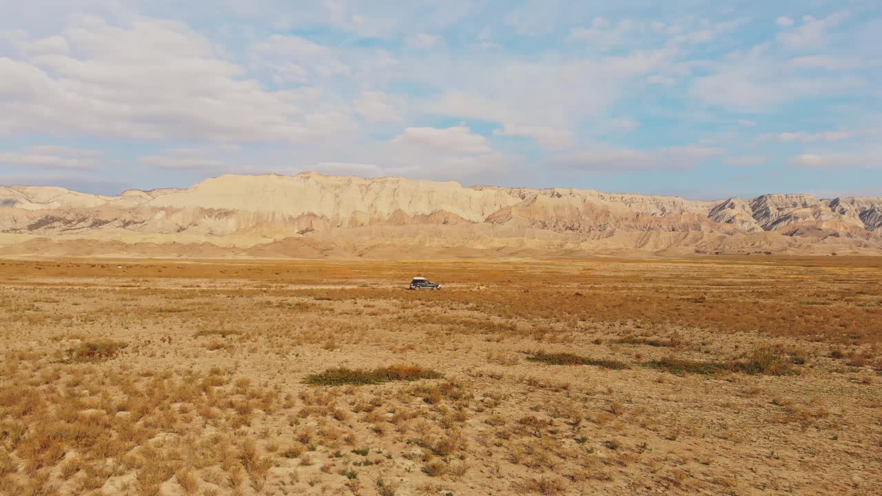 侧面鸟瞰图移动四轮驱动车辆在荒芜的地形与美丽的山背景。VAshlovani国家公园旅游视频素材