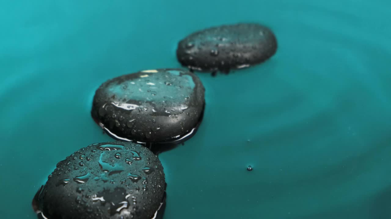 雨滴落在绿色的水中，落在黑色的石头上。视频素材