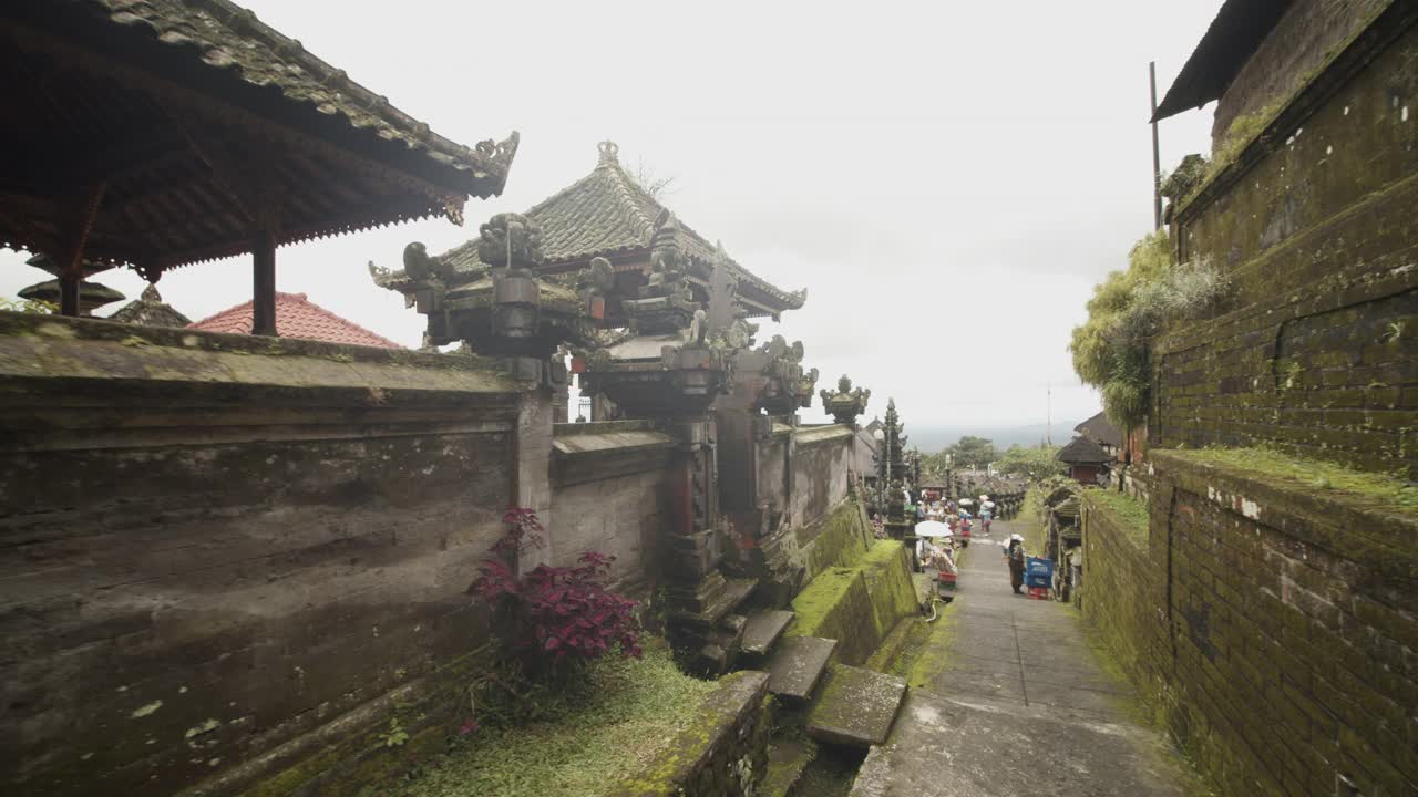 多莉拍摄了在巴厘岛的白沙基寺穿过狭窄的寺庙街道的游客和当地人出售纪念品和探索古老的寺庙视频素材