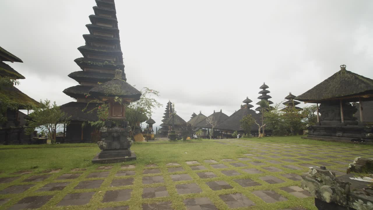 在印度尼西亚巴厘岛的贝萨基寺，多莉走过长满草的寺庙场地，那里有黑色的石头雕像和宗教建筑视频素材