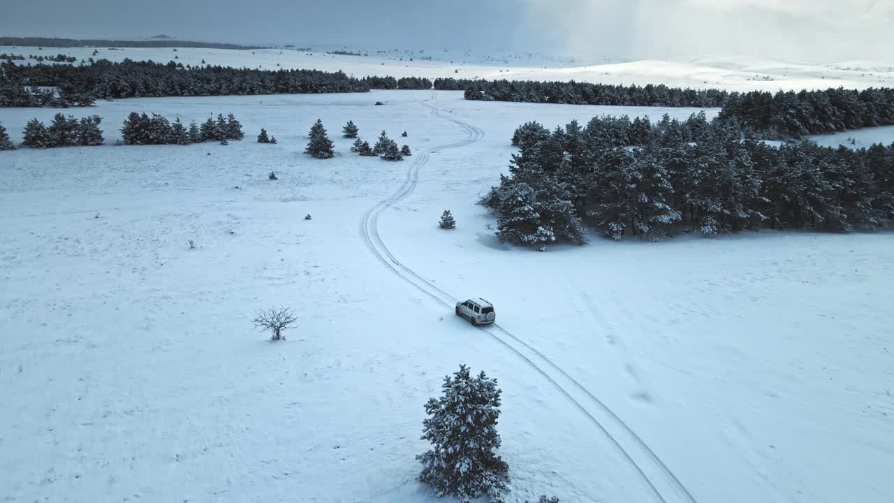 空中拍摄的白色汽车在被雪覆盖的道路上行驶视频素材