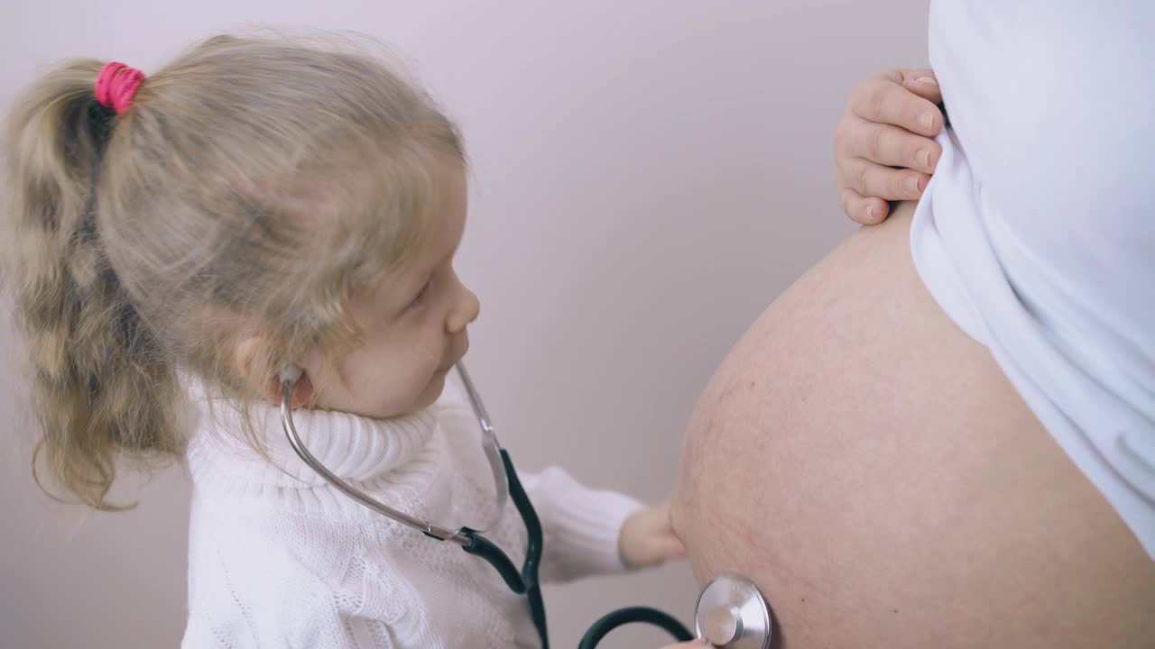 女孩用听诊器在怀孕妈妈肚子里听宝宝说话视频素材