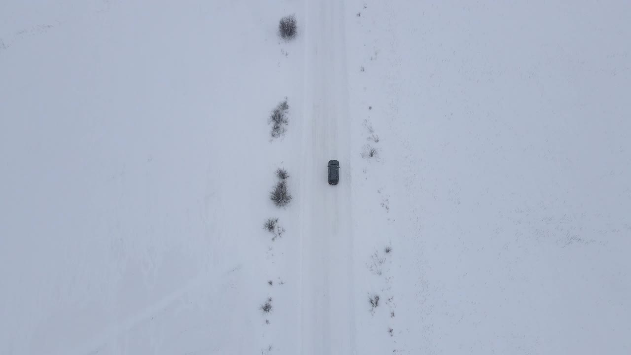 汽车在风雪中行驶。飘落的雪路雪花冬天的风暴。空中拍摄的汽车行驶在下雪的乡村道路上视频素材