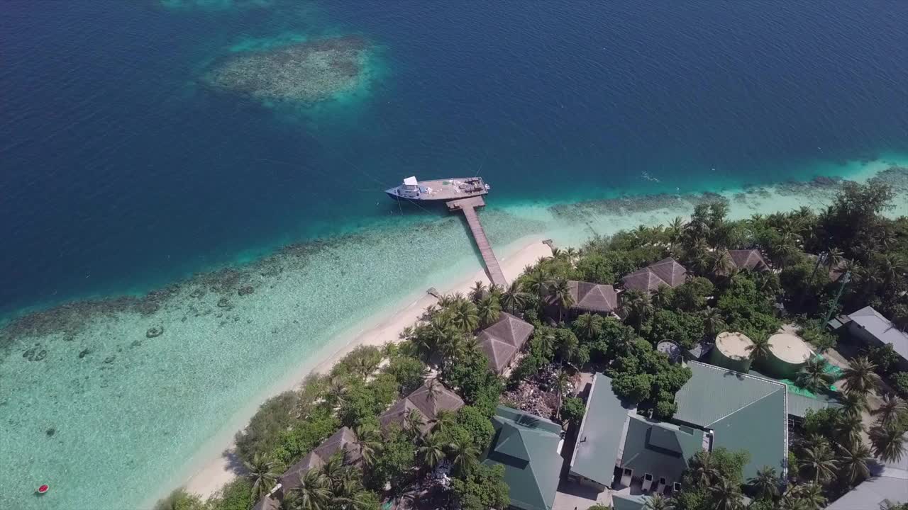 空中倾斜向下拍摄的船停泊在碧海码头，无人机向前飞行在度假胜地在阳光明媚的一天-瓦杜，马尔代夫视频素材